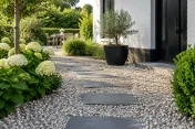 Pads van vierkante leisteenplaten door fijn wit grind naar voortuin met planten en potten