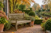 Verweerde houten tuinbank op herfstig terras naast planten en kanaalzicht