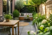 Kleine stedelijke tuin met houten tuinset, bank met kussens en veel groen
